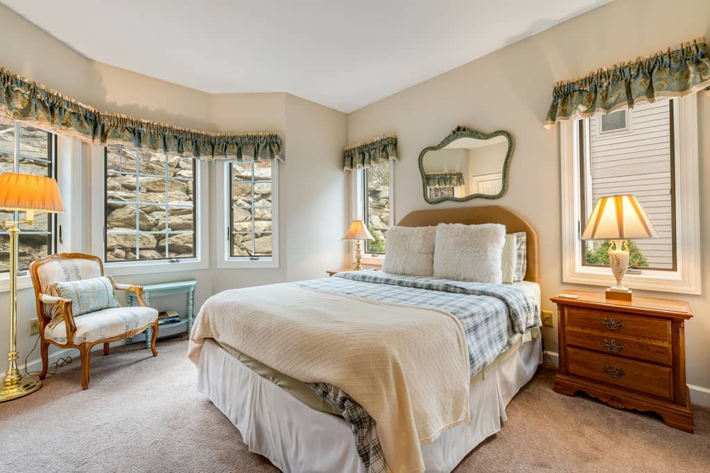 Une chambre à coucher avec un grand lit, deux lampes de chevet, une commode, une chaise et un miroir au mur.