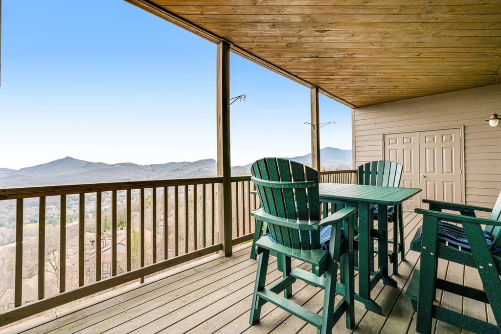 A covered outdoor area with a wooden deck, green Adirondack chairs, and a view of distant mountains.