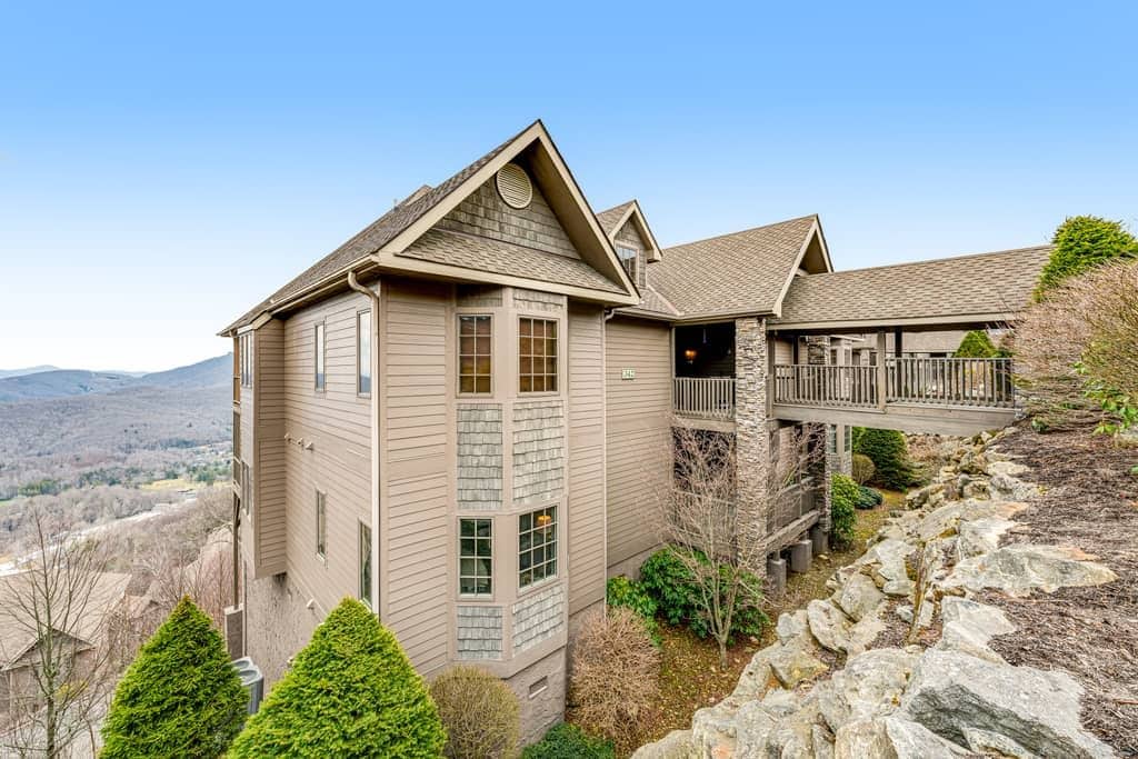 A two-story house with a stone foundation, a balcony, and a view of the mountains.