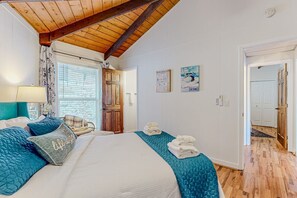 Ein Schlafzimmer mit einem großen Bett, einer Holzbalkendecke, einem Fenster mit Jalousien und einer Tür zu einem anderen Raum.
