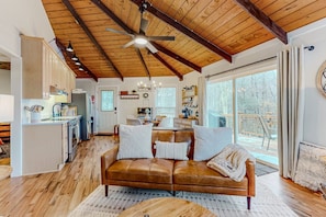 A spacious living area with a wooden ceiling, a leather sofa, and a large window providing a view of the outdoors. - The Beech Hut: 2br pet friendly roundhouse on Beech Mtn with hot tub, firepit, & fenced yard! (Beech Mountain)