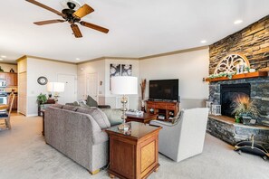 A living room with a fireplace, a ceiling fan, and a television. - A Sweet Escape: 2br Condo in The Reserve on Sugar Mtn - Long Range Views! (Sugar Mountain)