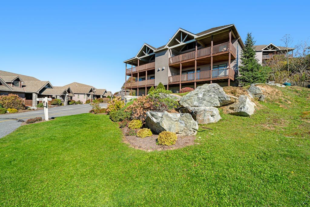 A multi-story building with a balcony on the second floor, surrounded by a well-maintained lawn and large rocks.