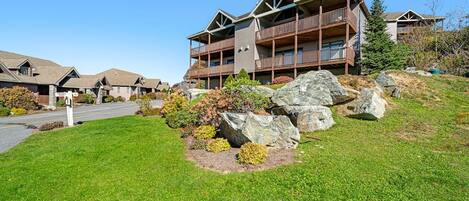 A multi-story building with a balcony on the second floor, surrounded by a well-maintained lawn and large rocks.