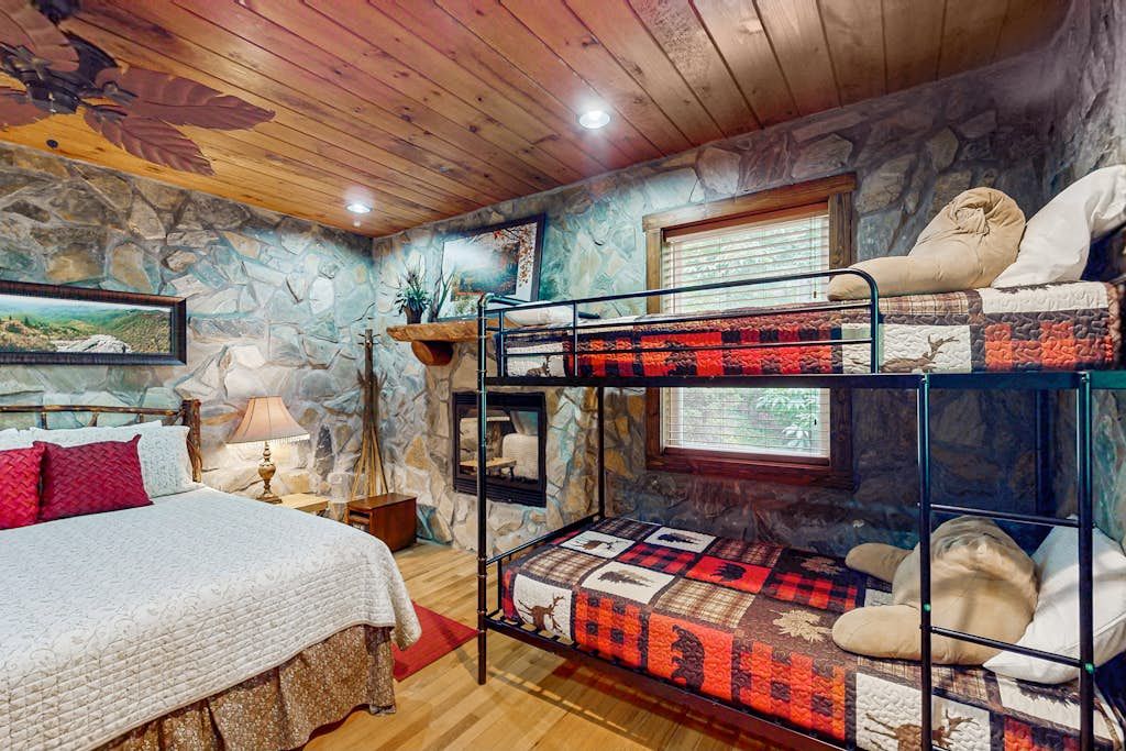 A bunk bed room with a stone wall, a wooden ceiling, and a bed with a white comforter.