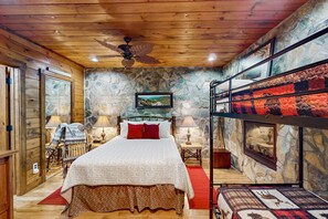 Un dormitorio con una cama nido, techo de madera, paredes de piedra, cama con colcha blanca y roja, y una alfombra roja.