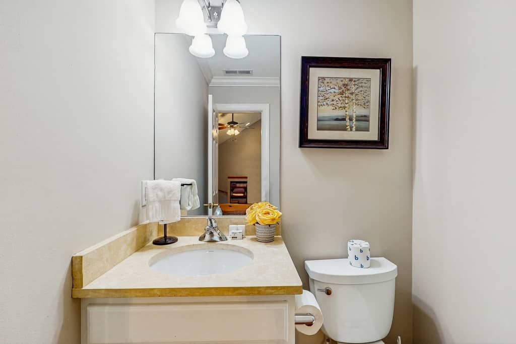 A bathroom with a sink, mirror, toilet, and a framed picture on the wall.