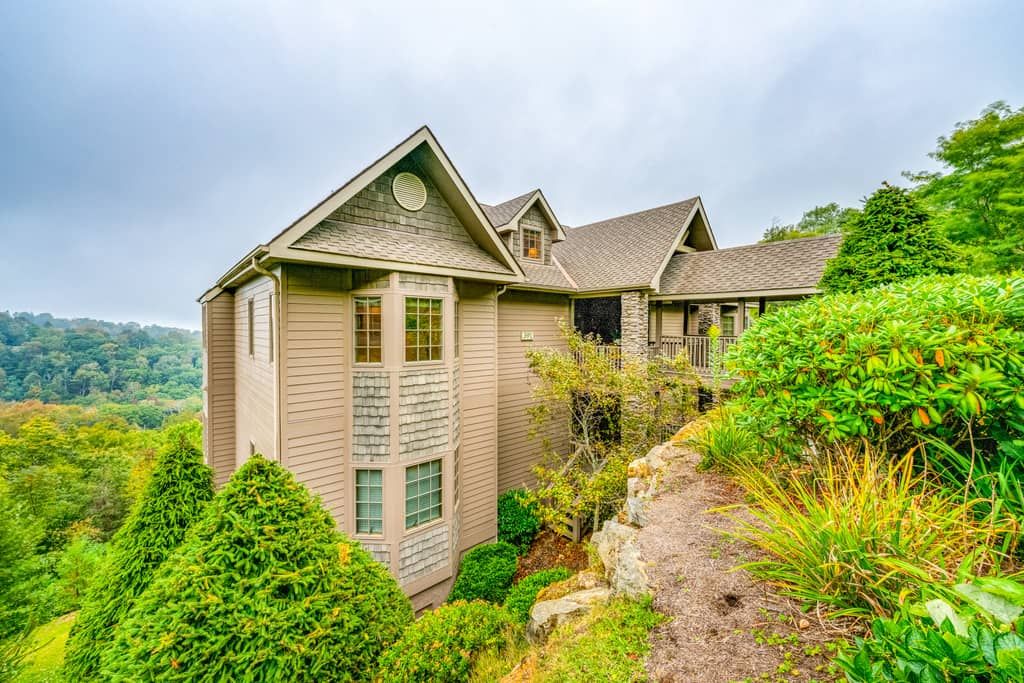 Uma casa com telhado em duas águas, cercada por vegetação exuberante e um terreno rochoso.
