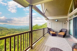 A covered deck with a view of a mountainous landscape, furnished with wicker chairs and a small table. - Sugar High at The Reserve II - Unobstructed Views (Banner Elk)