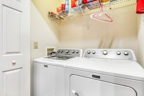 Ein Waschraum mit einer Maytag Waschmaschine und Trockner, einem Metallregal mit aufgehängter Kleidung und einer weißen Tür.