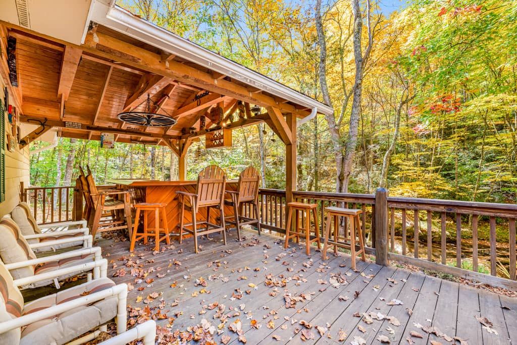 Eine Holzterrasse mit Sitzgelegenheiten und einem überdachten Bereich, umgeben von Bäumen im Herbstlaub.