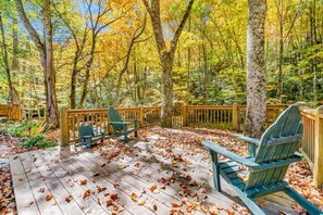 Eine Holzterrasse mit Adirondack-Stühlen, umgeben von Bäumen mit Herbstlaub.