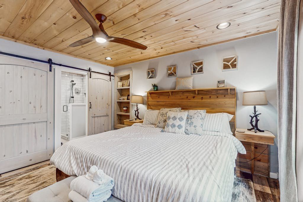 Une chambre à coucher avec un grand lit, une tête de lit en bois, des tables de chevet avec des lampes et un ventilateur de plafond.