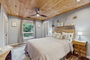 Un dormitorio con una cama grande, techo de madera y vistas al verdor exterior.