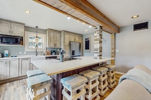 A kitchen with a central island, bar stools, wooden beams, and a stone accent wall. - Rotten Dog Getaway: Dog friendly slopeside 2br updated condo on Sugar Mtn! (Sugar Mountain)