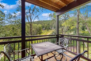 Un espacio de estar al aire libre cubierto, con una mesa y sillas, con vistas a un paisaje boscoso.