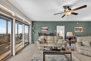 A spacious living room with a large window, a ceiling fan, and a cozy seating area. - Summit Serenity - Condo on Sugar Mountain with Amazing Views, Gas Fireplace, Walk to Slopes! (Banner Elk)