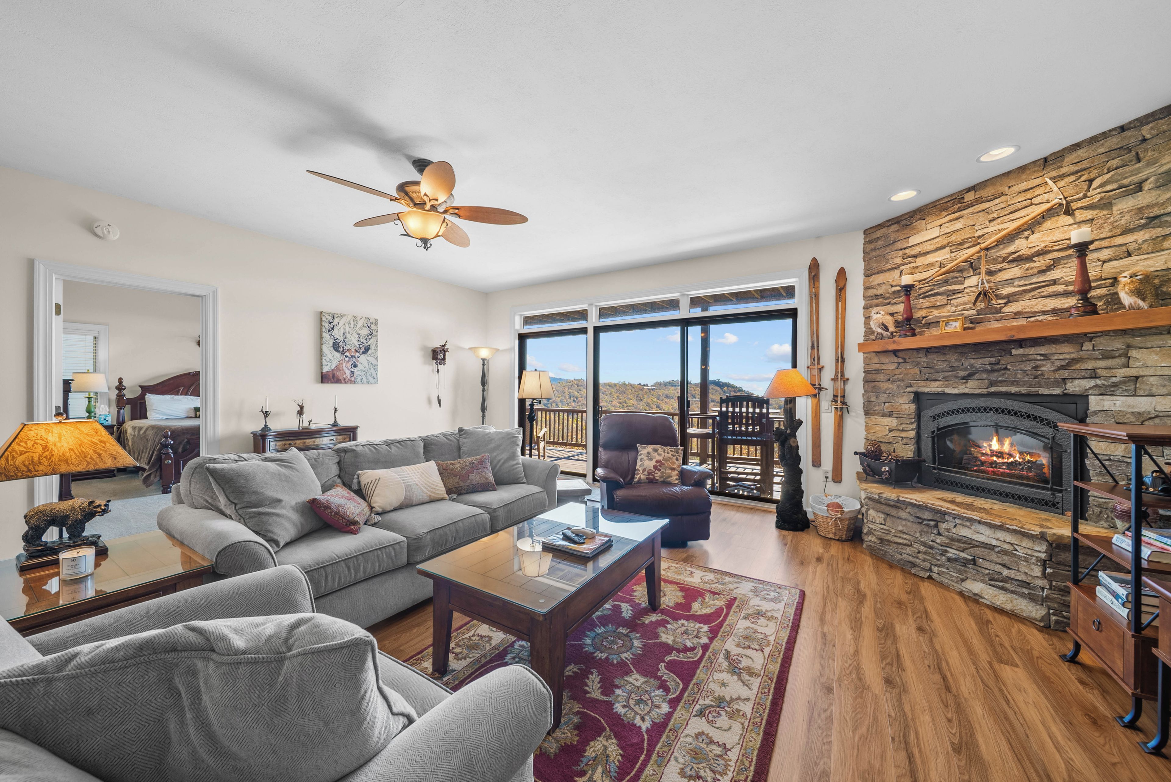 A spacious living room with a fireplace, a large sofa, a coffee table, and a view through the glass doors.