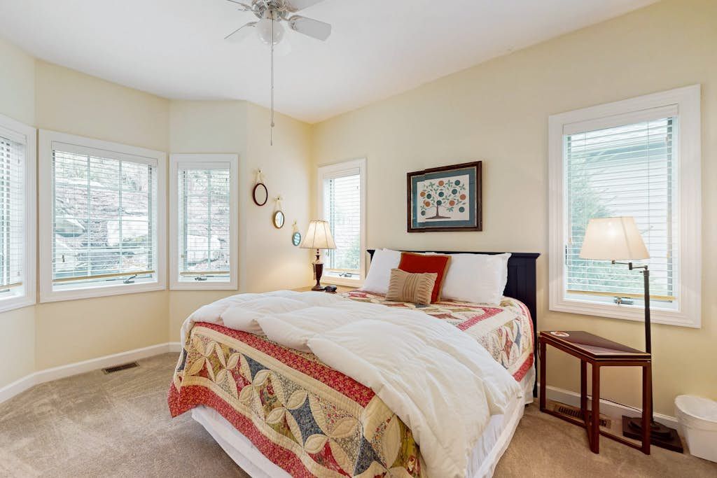 A bedroom with a large bed, multiple windows, a ceiling fan, and a framed picture on the wall.