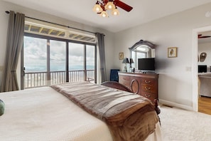 A bedroom with a large bed, a dresser, a television, and a balcony with a view. - The Owl's Nest at The Reserve- Condo on Sugar Mountain with Amazing Views, Gas Fireplace! (Banner Elk)