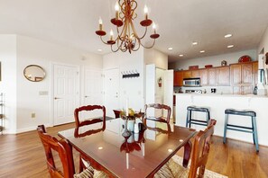 A dining area with a wooden table and chairs, a chandelier, and a kitchen in the background. - The Owl's Nest at The Reserve- Condo on Sugar Mountain with Amazing Views, Gas Fireplace! (Banner Elk)