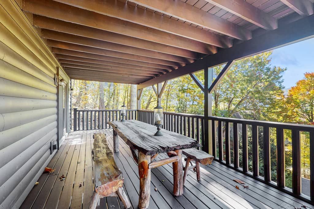 Terraza de madera con una mesa y bancos, con vistas a una zona boscosa.