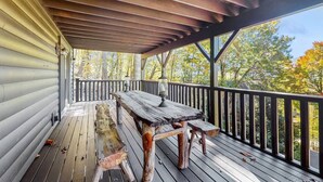 Een houten terras met een tafel en banken, met uitzicht op een bebost gebied.