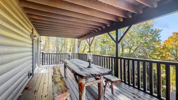 A wooden deck with a table and benches, overlooking a forested area.