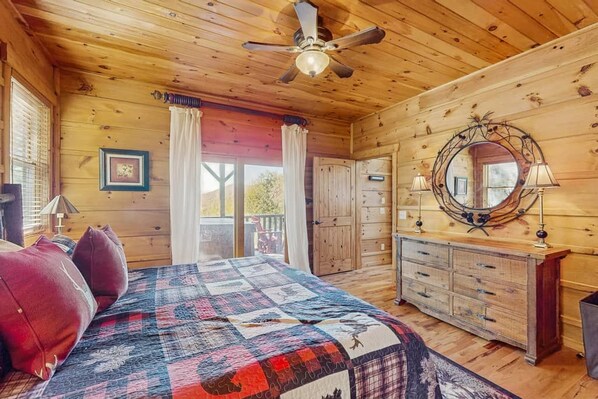 A wooden cabin interior with a bed, dresser, and a ceiling fan.