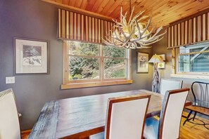 A dining area with a large wooden table, chairs, and a chandelier with antlers. - Howling Rock - Mtn Views, Hot Tub, Pool Table + More (Banner Elk)