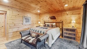 Een slaapkamer in een blokhut met een bed, een stoel, een nachtkastje en een wandlamp.