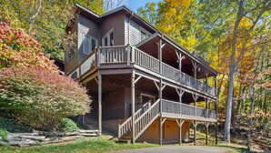 Een houten chalet met twee verdiepingen en een balkon, omgeven door herfstbladeren.