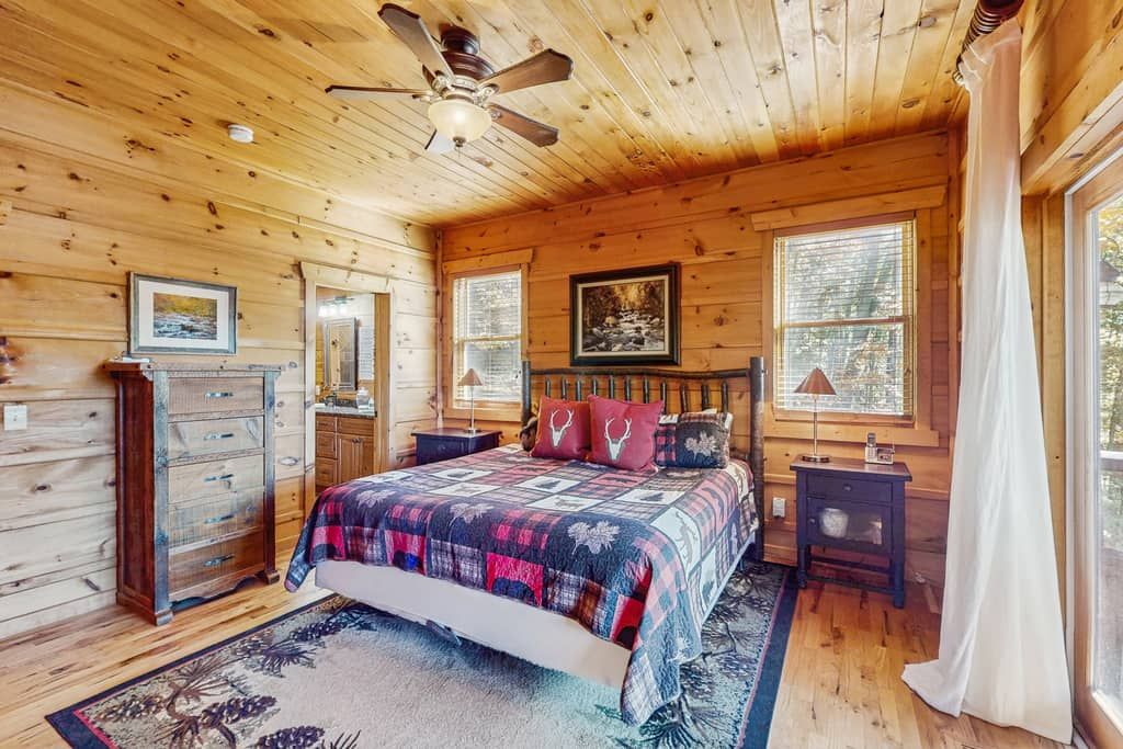 A wooden cabin bedroom with a bed, dresser, and a ceiling fan.