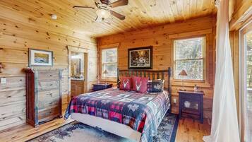 A wooden cabin bedroom with a bed, dresser, and a ceiling fan.
