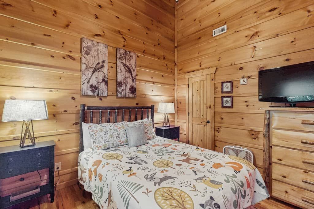 A wooden cabin room with a bed, a television, and a dresser.