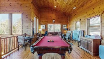 A wooden cabin with a pool table, seating area, and large windows.