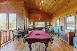 A wooden cabin with a pool table, seating area, and large windows.