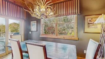 A dining area with a large table and chairs, a chandelier, and a window with a view of greenery.