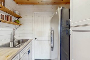 A compact kitchen with a stainless steel sink, a white door, and a refrigerator.