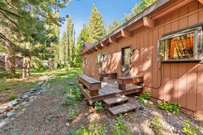 A wooden cabin with a deck and a small table. - Happy Hideaway on the West Shore by Tahoe Getaways - 4BR + Private Beach Access Near Tahoe City (Tahoe City)