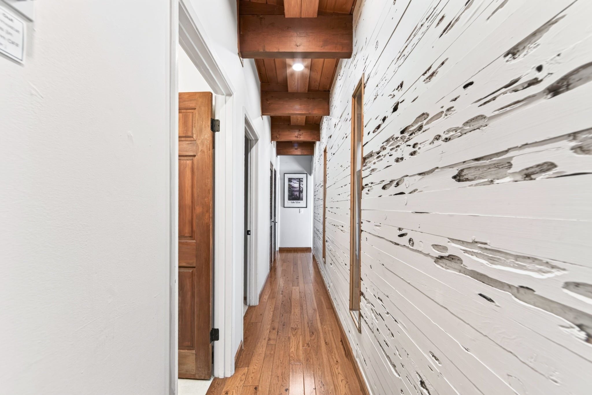 Ein Korridor mit Holzboden, weißen Wänden und einer Holzkονstruktion an der Decke.