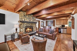 A cozy living room with a stone fireplace, leather furniture, and wooden beams. - Happy Hideaway on the West Shore by Tahoe Getaways - 4BR + Private Beach Access Near Tahoe City (Tahoe City)