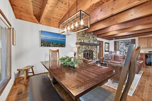 A dining area with a wooden table, chairs, a fireplace, and a stone wall. - Happy Hideaway on the West Shore by Tahoe Getaways - 4BR + Private Beach Access Near Tahoe City (Tahoe City)