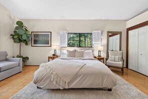 A bedroom with a large bed, bedside tables, a chair, a plant, and a window with shutters. - Happy Hideaway on the West Shore by Tahoe Getaways - 4BR + Private Beach Access Near Tahoe City (Tahoe City)