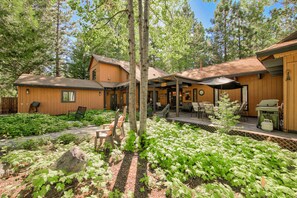 A wooden cabin with a patio area, surrounded by lush greenery and trees. - Happy Hideaway on the West Shore by Tahoe Getaways - 4BR + Private Beach Access Near Tahoe City (Tahoe City)
