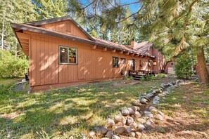 A wooden cabin with a covered porch, surrounded by trees and a stone pathway. - Happy Hideaway on the West Shore by Tahoe Getaways - 4BR + Private Beach Access Near Tahoe City (Tahoe City)