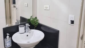 A bathroom with a white sink, a mirror, a black countertop, and a potted plant. - XYZ’s Condo-One Palm Tree Villas, Newport: 6-Min Walk to NAIA T3 via Runway MNL (Unknown)
