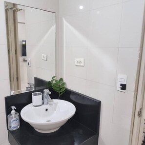 A bathroom with a white sink, a mirror, a black countertop, and a potted plant. - XYZ’s Condo-One Palm Tree Villas, Newport: 6-Min Walk to NAIA T3 via Runway MNL (Unknown)