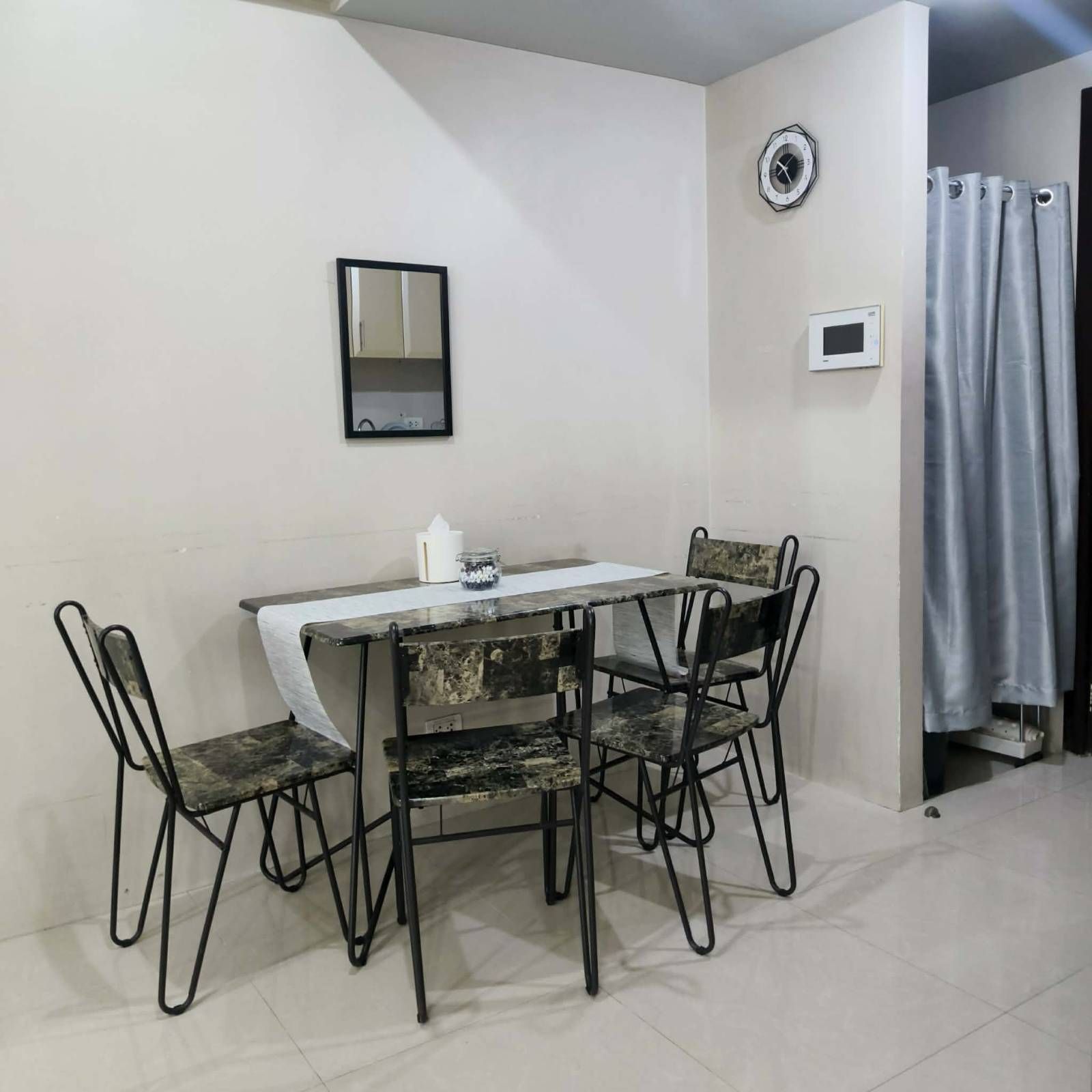 A small dining area with a table and four chairs, a clock, and a curtain on the wall.