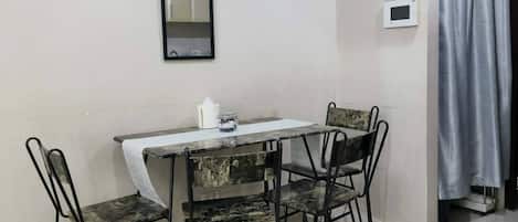 A small dining area with a table and four chairs, a clock, and a curtain on the wall.